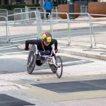 A dedicated athlete competes in a marathon using a racing wheelchair on city streets.